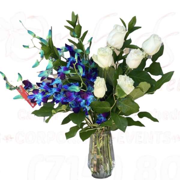 White roses and blue orchids in a clear glass vase