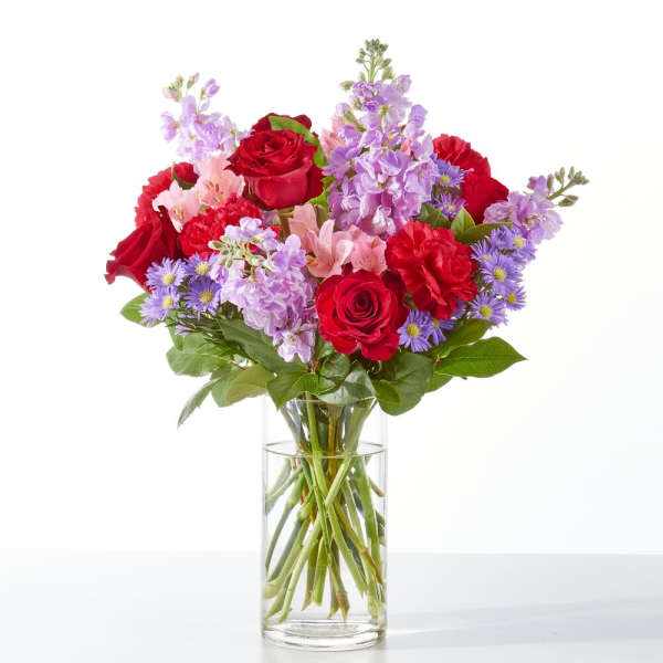 Bouquet of red roses, purple flowers, and pink blooms in a clear glass vase