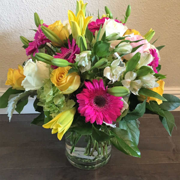 Mixed bouquet of roses, lilies, and gerbera daisies in a glass vase