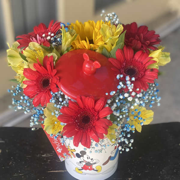 Bright mixed bouquet in a Mickey Mouse bucket with red, yellow, and blue flowers
