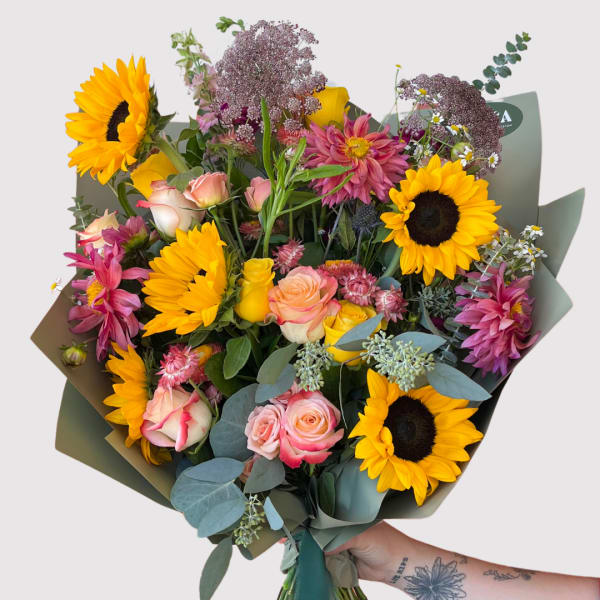 Bouquet of sunflowers, roses, and pink dahlias wrapped in paper