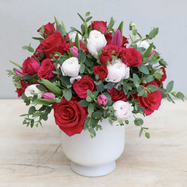 Red and white rose and ranunculus arrangement with pink accents in a white vase