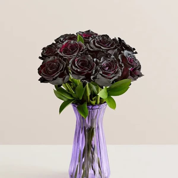 Dark roses arranged in a purple glass vase
