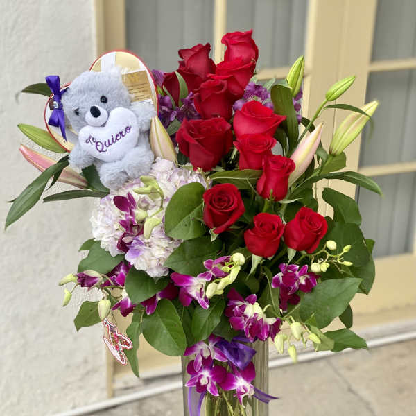 Red roses and purple orchids in a clear vase with a teddy bear