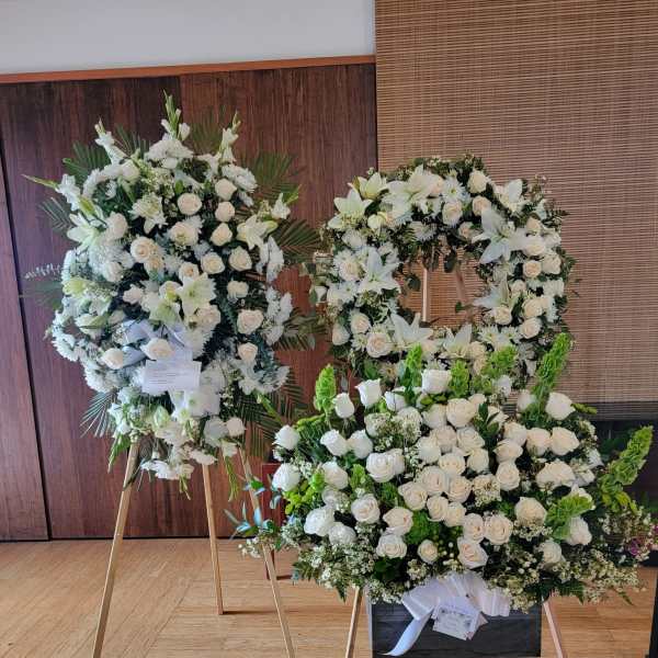 White floral funeral wreaths on stands with roses and lilies