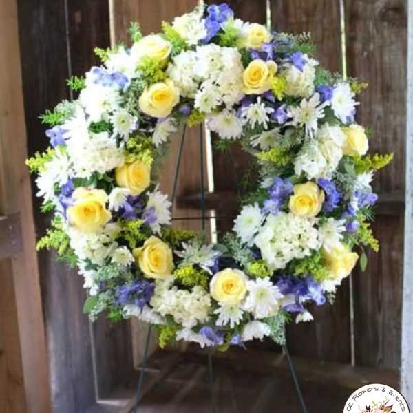 Standing wreath of yellow roses, white daisies, and purple flowers on a metal easel