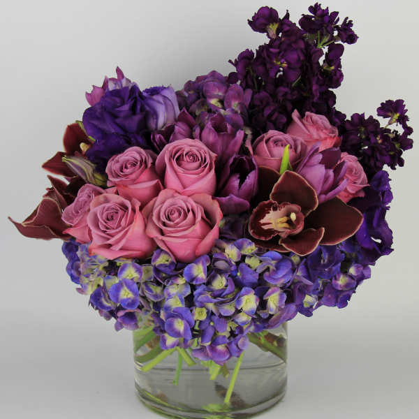 Pink roses and purple flowers arranged in a clear glass vase