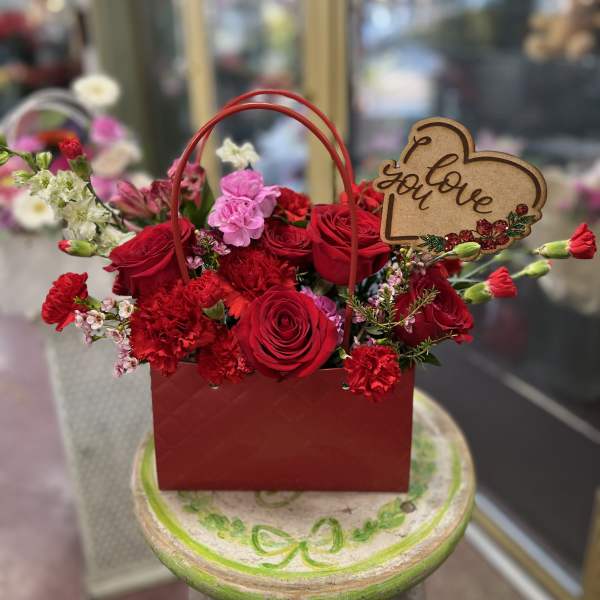 Red rose and carnation arrangement in a red handled gift box with a love sign