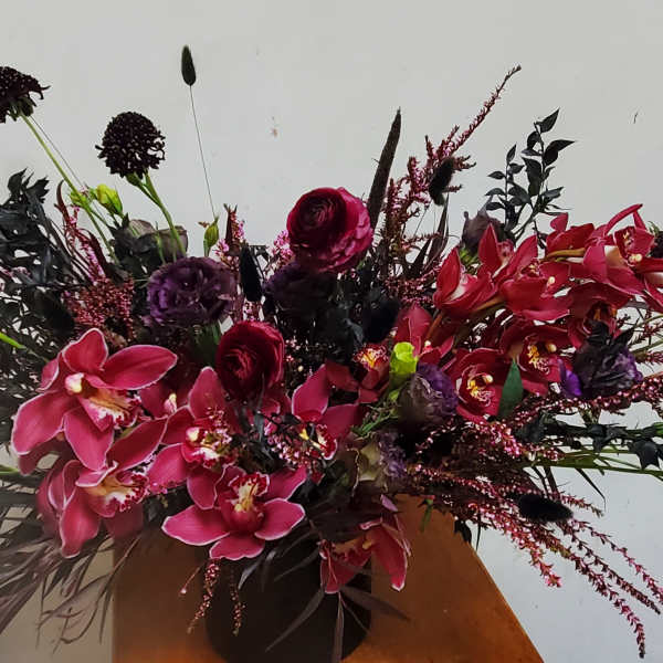 Large arrangement of pink orchids and dark red flowers in a vase