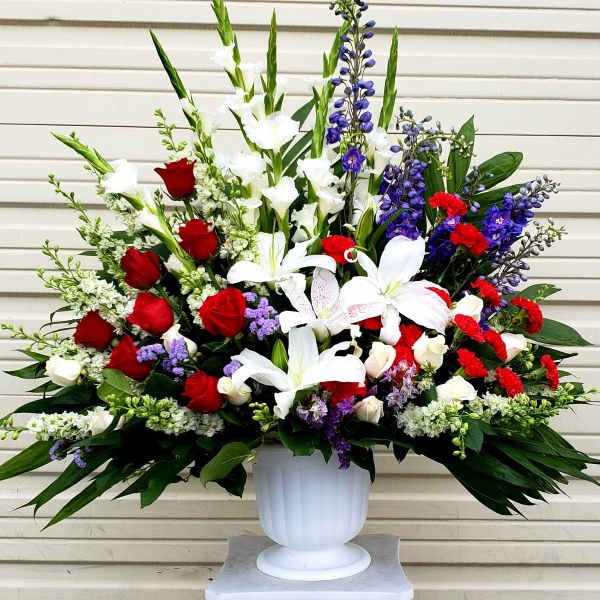 Large arrangement of red roses, white lilies, and purple flowers in a white urn