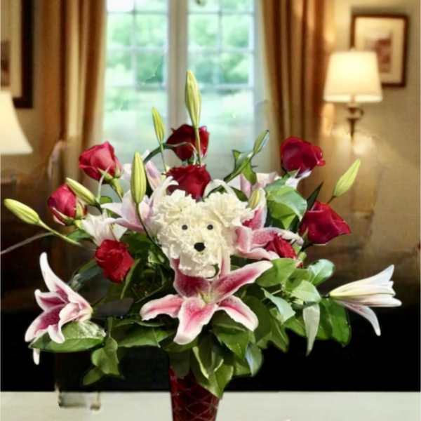 Bouquet of red roses and pink lilies in a red vase with a teddy bear center