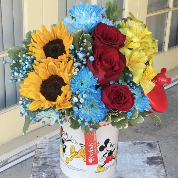 Bouquet of sunflowers, red roses, blue chrysanthemums, and yellow alstroemeria in a Mickey Mouse tin