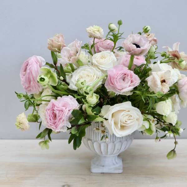 Low arrangement of pink and ivory roses and ranunculus in a white pedestal bowl
