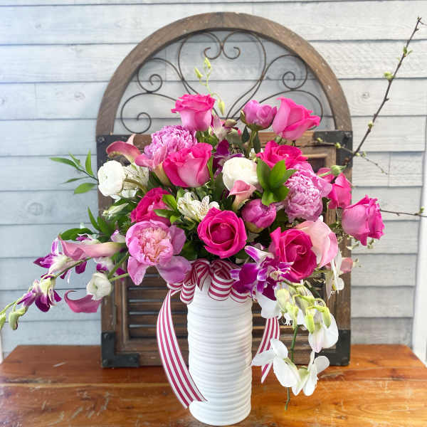 Pink and white floral arrangement in a white vase with striped ribbon