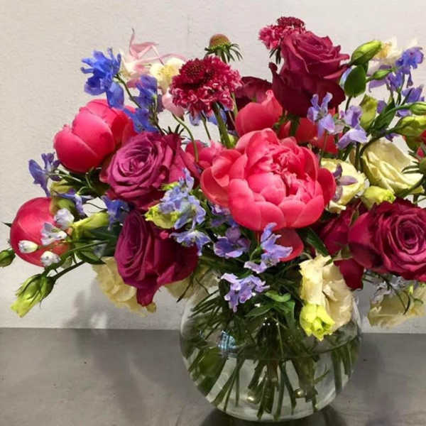 Mixed bouquet of pink, purple, and blue flowers in a clear glass vase