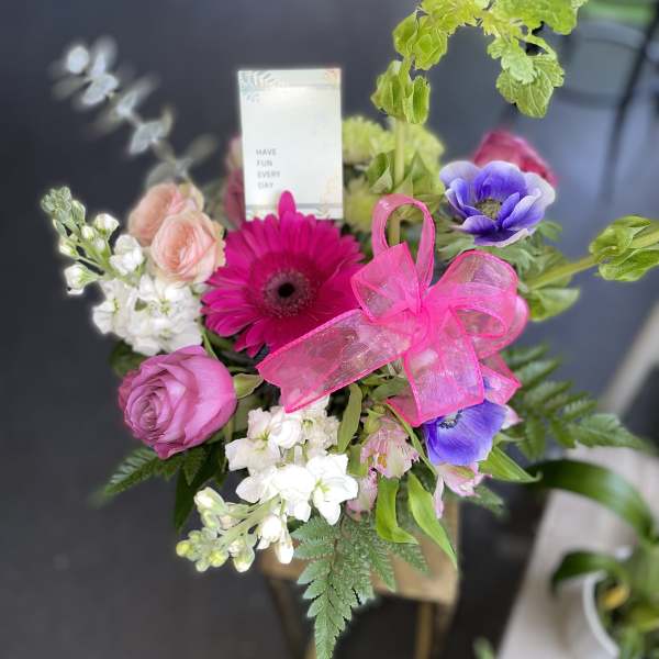 Mixed bouquet with pink, purple, and white flowers tied with a bright pink bow