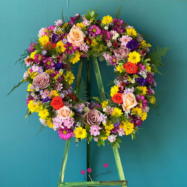 Colorful floral wreath on a standing easel against a teal background