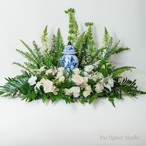 White roses and greenery arranged around a blue-and-white ceramic urn