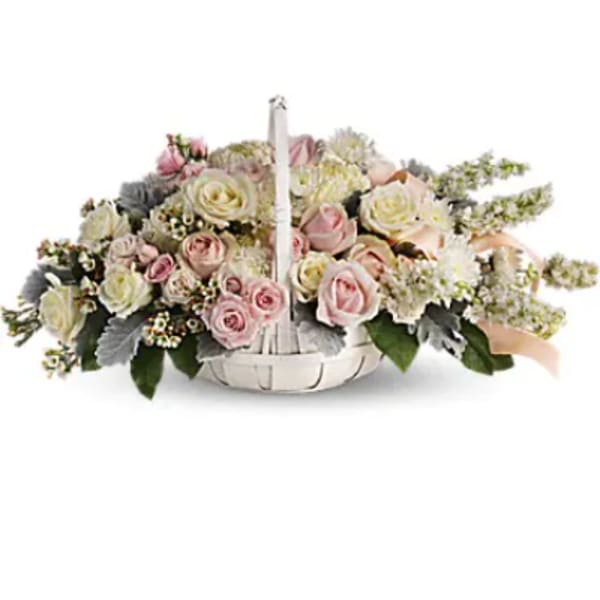 Low basket arrangement of pale pink and cream roses with white accent flowers and a peach ribbon