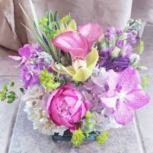 Mixed bouquet with pink calla lilies, orchids, and a peony in a low container
