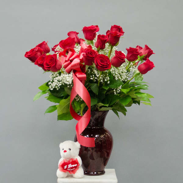 Red roses in a dark vase with a pink ribbon and teddy bear