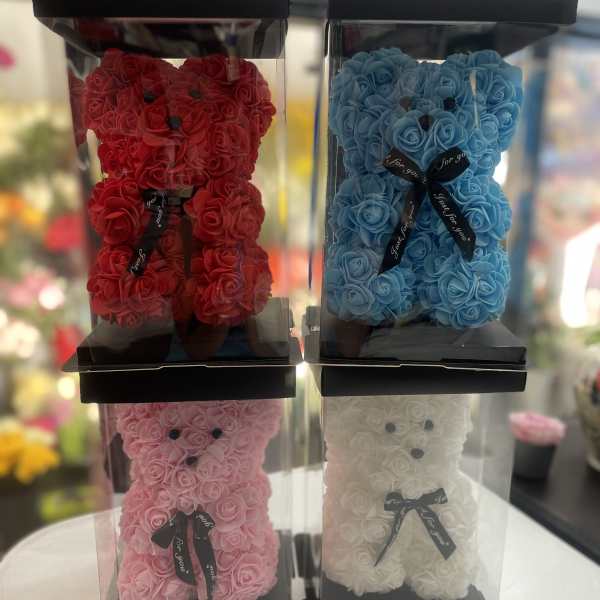 Four rose teddy bears in clear display boxes, in red, blue, pink, and white.