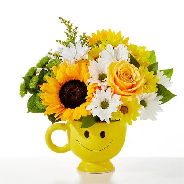 Yellow mug vase with a smiley face holding sunflowers, roses, and daisies