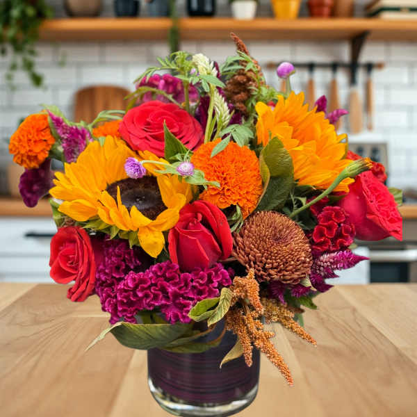 Mixed bouquet of sunflowers, red roses, and orange blooms in a glass vase