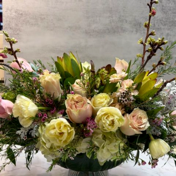 Low compote arrangement of cream and blush roses with pastel blooms in a green pedestal bowl
