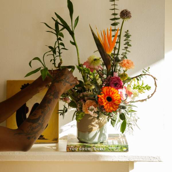 Colorful mixed flower arrangement with bird of paradise and orange gerbera daisies in a ceramic vase.
