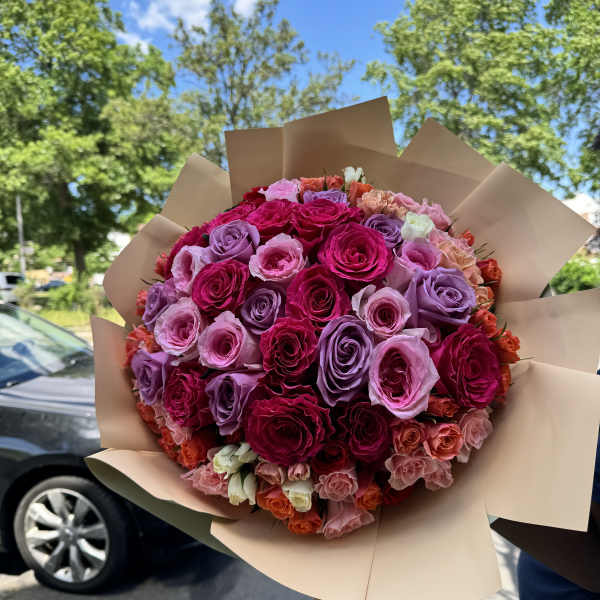 Large bouquet of pink, purple, and red roses wrapped in tan paper