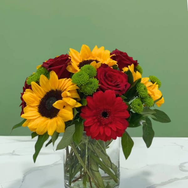 Bouquet of sunflowers, red roses, and a red gerbera daisy in a glass vase