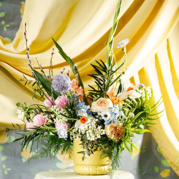 Colorful mixed flower arrangement in a yellow vase on a draped table