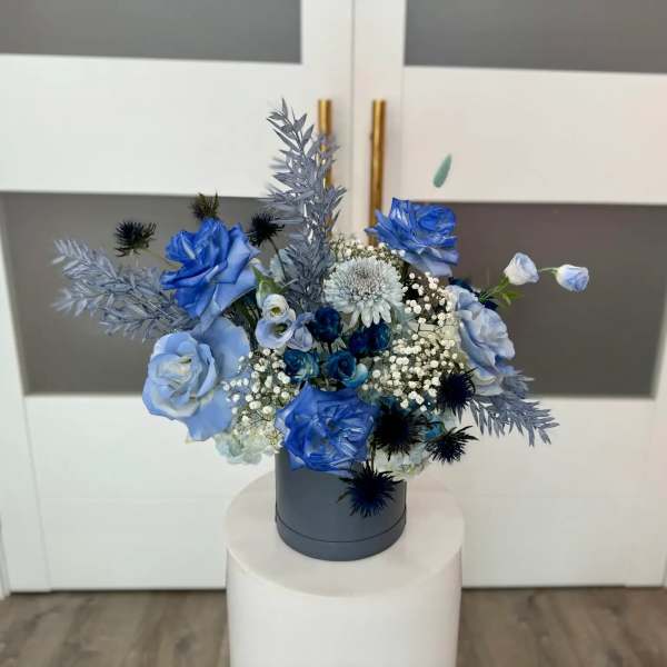 Blue rose arrangement in a gray hatbox with white filler flowers
