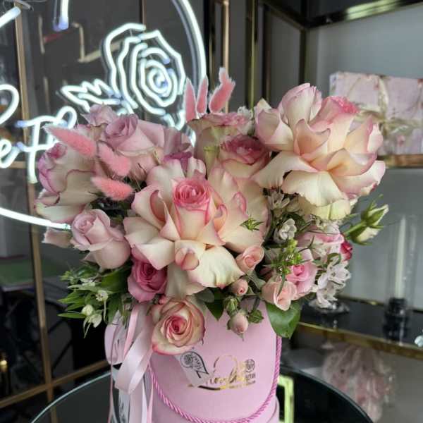 Pink and cream roses arranged in a round pink box with ribbon.