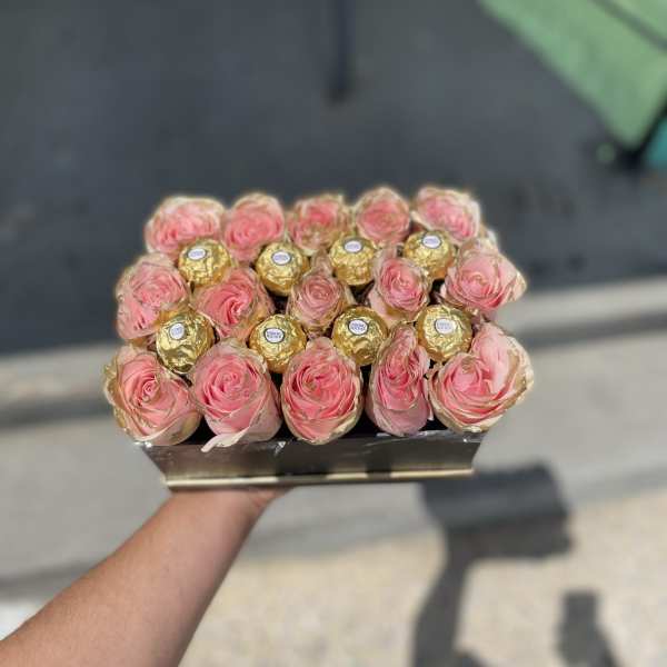 Pink roses arranged with gold-wrapped chocolates in a small box