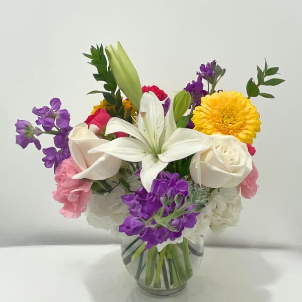 Mixed bouquet in a clear glass vase with white lilies, roses, and purple blooms
