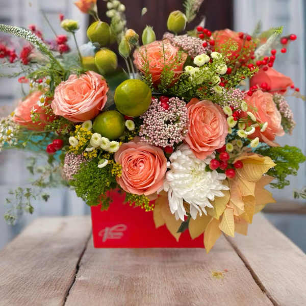 Peach roses and mixed blooms arranged in a red box with berries