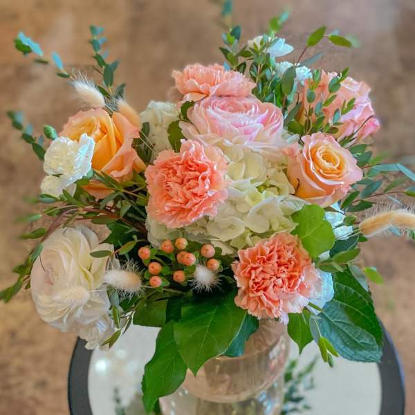Peach and white bouquet with roses, carnations, and hydrangea in a glass vase