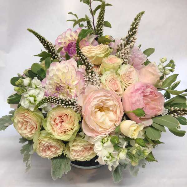 Pastel bouquet of roses, dahlias, and white flowers in a low container