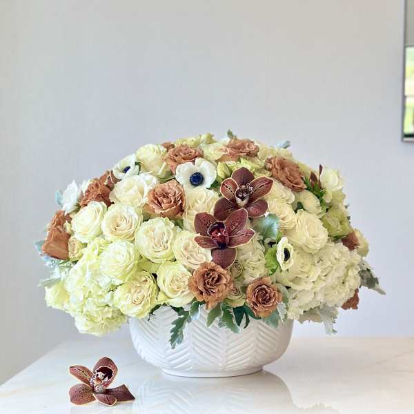 Cream and peach floral arrangement in a white bowl vase with burgundy orchids
