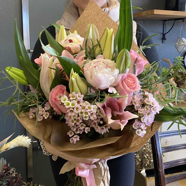 Large bouquet of pink roses, lilies, and peonies wrapped in brown paper