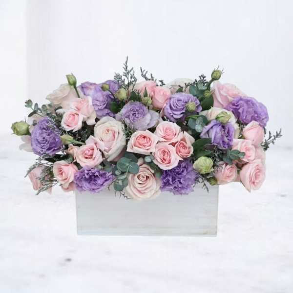 Low arrangement of pink roses and lavender lisianthus in a white rectangular wooden box