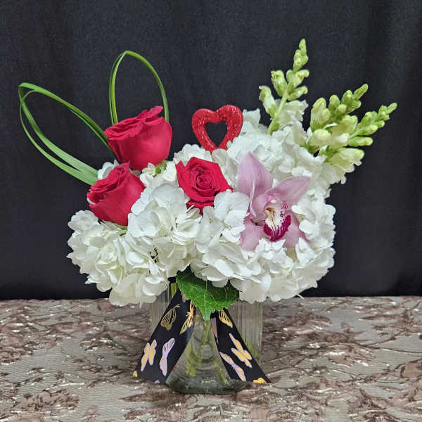 Pink roses and white hydrangeas in a glass vase with an orchid accent
