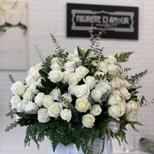 Large white rose arrangement in a round white box with greenery