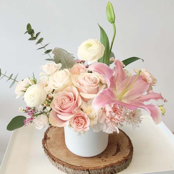 Pink and white floral arrangement in a white vase with a pink lily