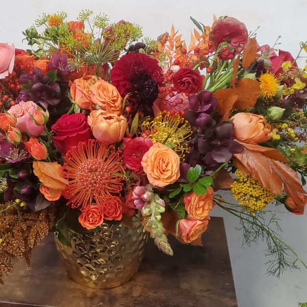 Large autumn bouquet with orange, red, and pink flowers in a gold vase