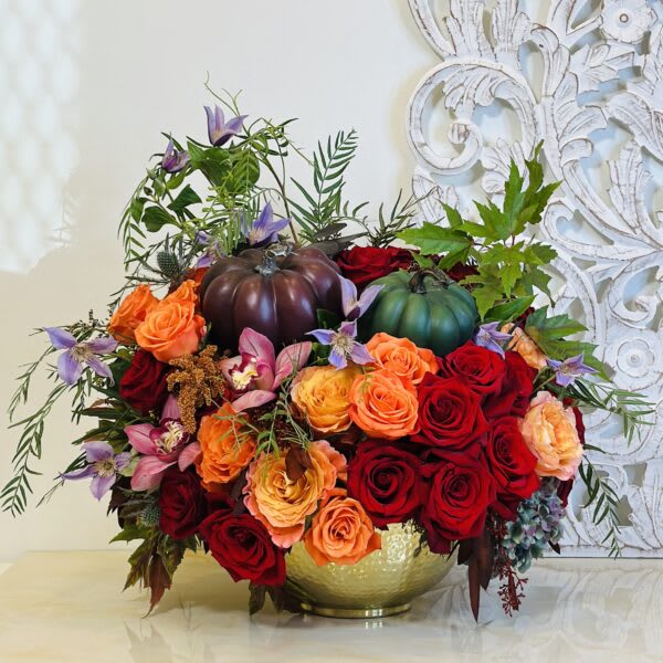 Arrangement of red and orange roses with decorative pumpkins in a gold bowl