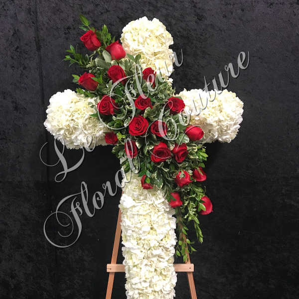 Cross-shaped floral tribute with red roses and white hydrangeas on an easel