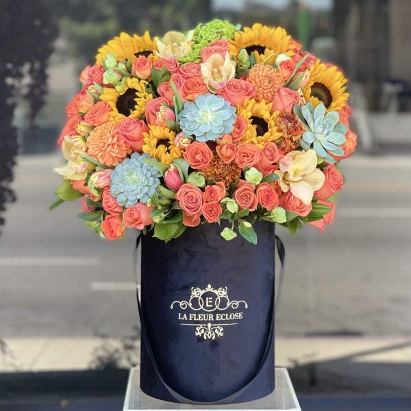 Large bouquet of coral roses, sunflowers, and blue succulents in a navy hat box